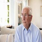 Senior Man Sitting On Sofa At Home Suffering From Dementia