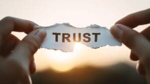 A woman’s hands hold a fragile piece of paper with the word Trust showing that trust is broken when betrayal occurs.