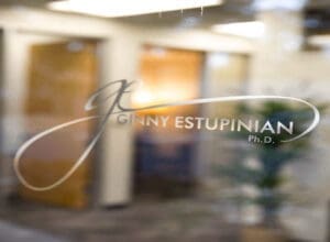 Close-up image of the front door logo of Ginny Estupinian, PhD, Los Gatos Psychologist, featuring the official logo prominently displayed on the glass. Through the door, the welcoming lobby is visible, showcasing warm lighting, comfortable seating, and tasteful decor, creating an inviting atmosphere
