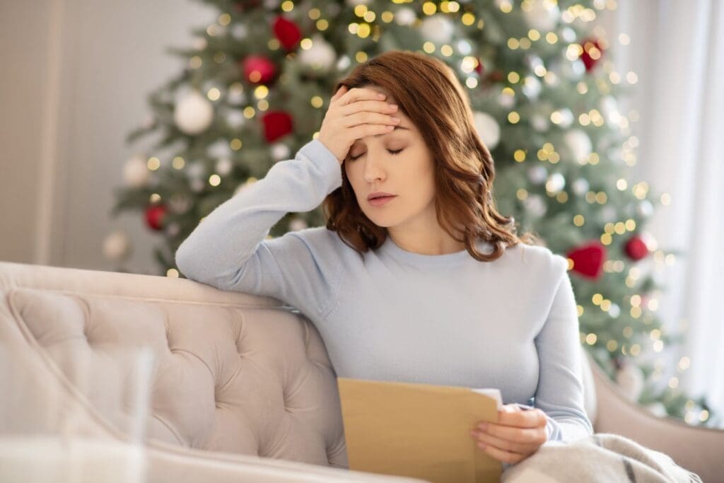 A woman holding a holiday invitation and looking overwhelmed, symbolizing how Dr. Ginny Estupinian, PhD, helps individuals manage holiday stress and emotional overload