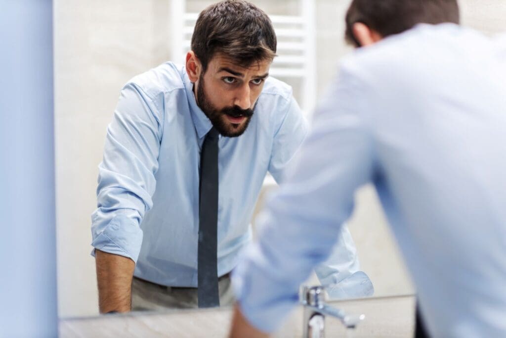 Business owner looking into a mirror, symbolizing leadership self-reflection and organizational insight guided by Dr. Ginny Estupinian, PhD